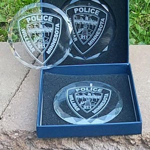 May include: Two clear glass ornaments with a diamond-shaped pattern. Each ornament features a white engraved police badge with the text "Police Willmar Minnesota 911". The ornaments are displayed in blue velvet boxes.