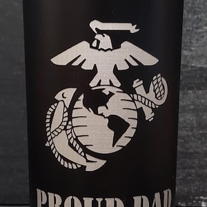 May include: Black stainless steel can cooler with a silver engraved Marine Corps emblem and the words "PROUD DAD" and "FrostBuddy."