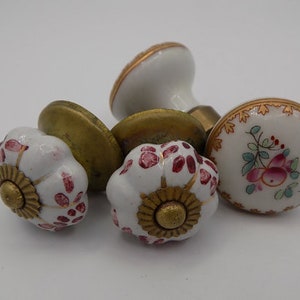 May include: Set of four porcelain cabinet knobs with gold accents. Two knobs feature a floral design with pink and green accents, and two knobs feature a red and gold floral design.