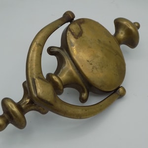 May include: A brass door knocker with a decorative design. The knocker is shaped like a bell with a ring handle and a decorative finial.