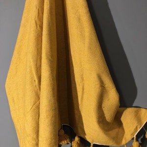 May include: A mustard yellow throw blanket with white pom-poms along the bottom edge.