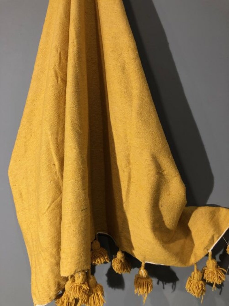 May include: A mustard yellow throw blanket with white pom-poms along the bottom edge.