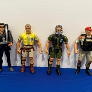 Pode incluir: Quatro figuras de ação em várias roupas. Uma figura usa um fato de mergulho preto com um tanque de mergulho, outra tem um colete amarelo, uma terceira usa um uniforme verde com uma máscara de gás e a última tem um boné vermelho e um colete preto.