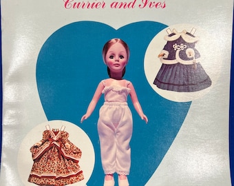 May include: A paper doll with six outfits. The doll is wearing a white dress and pants. The outfits include a brown and white floral dress, a blue dress with white trim, and a white dress with a blue sash. The doll is from the Effanbee brand and is a Currier and Ives product.