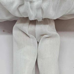 May include: A vintage doll's lower body, featuring white linen pants with lace trim at the ankles. The doll's legs end in gold-colored shoes with clear heels. The doll's skirt is made of a sheer, white fabric.