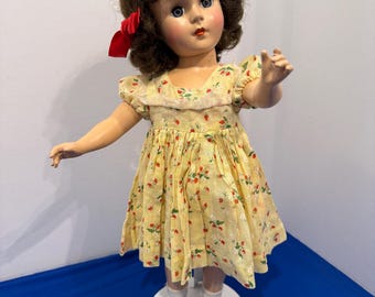 Bambola vintage anni '50 in plastica rigida, alta 45 cm, senza marchio, con capelli castani e vestito con stampa di fragole.