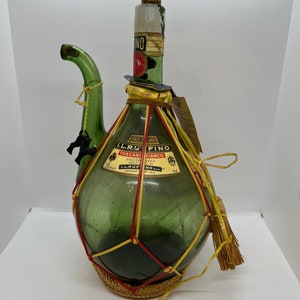 Könnte beinhalten: Eine grüne Glasflasche mit einer geflochtenen Strohüberzug und einem roten und gelben Etikett mit der Aufschrift "IL.RUFFINO. TOSCANA BIANCO. VINO DA TAVOLA. PROD. E IMB. IL.RUFFINO.  FONTANELLE - FIRENZE.  N.O. 24."