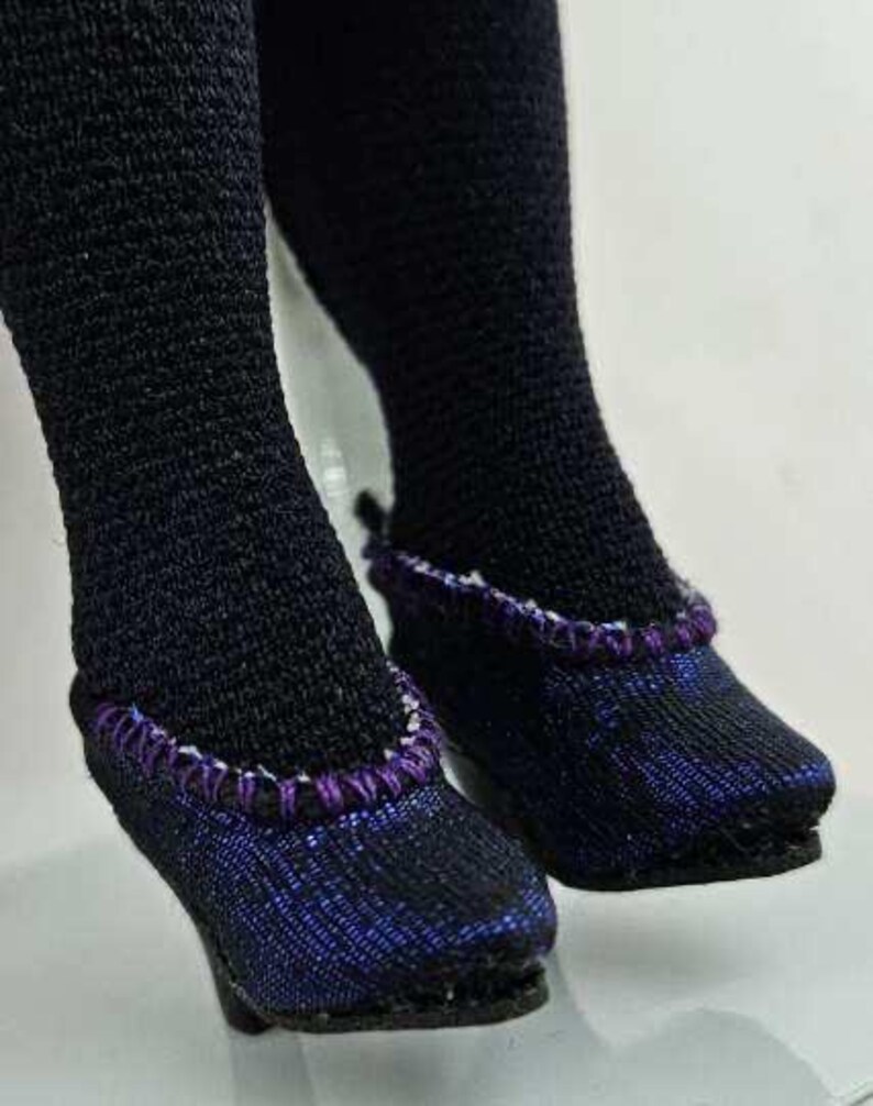 May include: Close-up of black doll stockings and shoes. The shoes are black with a purple and white trim. The shoes have a slight heel. The stockings are black.
