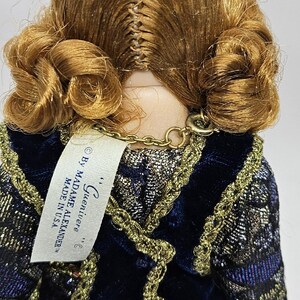 May include: A vintage doll with auburn hair styled in curls. The doll wears a dark blue velvet dress with gold trim. A tag reads "...Guenivere... By Madame Alexander MADE IN USA."