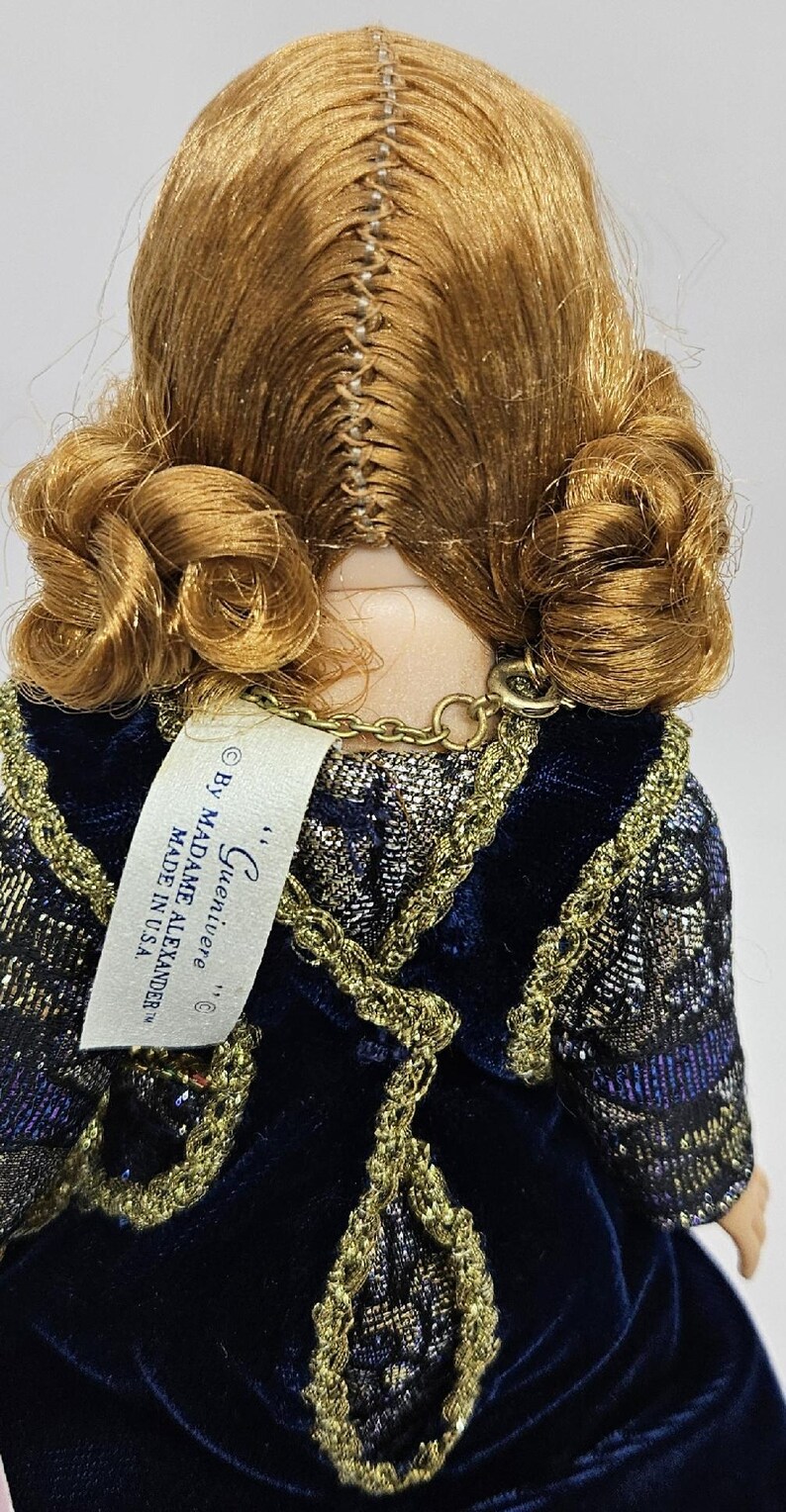 May include: A vintage doll with auburn hair styled in curls. The doll wears a dark blue velvet dress with gold trim. A tag reads "...Guenivere... By Madame Alexander MADE IN USA."