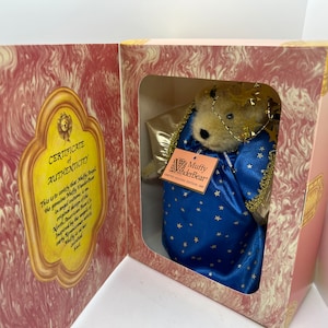 Può includere: Un orsetto angelo Muffy VanderBear in una scatola decorativa. L'orsetto indossa una veste di raso blu con stelle e finiture dorate e un'aureola dorata. La scatola ha un motivo marmorizzato rosa e crema e un certificato di autenticità.