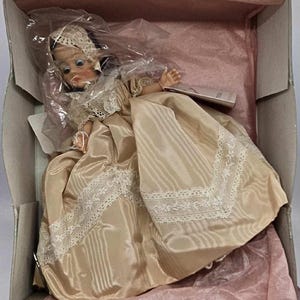 May include: A vintage doll in a box, dressed in a satin gown with lace trim. The doll has a bonnet and is packaged in a box with pink tissue paper.