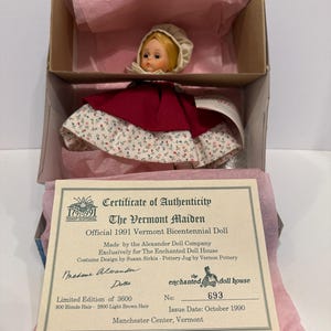 May include: A vintage doll, "The Vermont Maiden," in its original box. The doll has blonde hair and is wearing a red cape and a floral print dress. The box includes a certificate of authenticity from The Enchanted Doll House.
