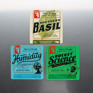 May include: Three square-shaped craft beer labels with a green, blue, and white background. The labels feature the Fullsteam Brewery logo and the names of the beers: "Southern Basil", "Humidity", and "Rocket Science".