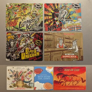 May include: A set of ten colorful beer coasters featuring illustrations of mythical creatures, including a lizard king, a ninja unicorn, a blood of the unicorn, a goat, and a unicorn riding a chai. The coasters are made of a durable material and are perfect for protecting your furniture from spills.