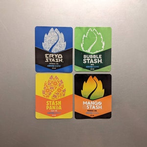 May include: Four square stickers with different designs. Each sticker features a green, yellow, or blue leafy design with the text "Cryo Stash" and the type of beer. The stickers are for Cryohops Imperial IPA, Cryohops IPA, Cryohops Hazy IPA, and Cryohops Mango IPA.