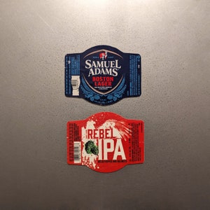 May include: Two beer bottle labels. The top label is blue and red with the text "Samuel Adams Boston Lager" and the bottom label is red with the text "Rebel IPA Boldly Hopped and Balanced".