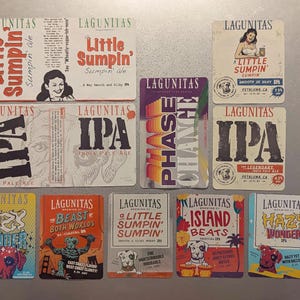 May include: A collection of 12 colorful coasters featuring various designs and text, including "Lagunitas", "Little Sumpin'," "IPA", "Phase Change", "Island Beats", "Hazy Wonder", and "Beast Both Worlds".