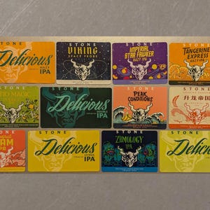 May include: A collection of 12 Stone Brewing Company beer labels featuring various designs and names, including "Delicious", "Viking", "Imperial", "Tangerine Express", "Patio Magic", "Peak Conditions", "升龙帝国", "Grapefruit Slam", "Zumology", and "Delicious".