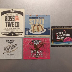May include: Five different beer coasters with colorful designs and text. The coasters feature names like "Boss Tweed", "Blueberry Maple Stout", "Dank Juice", "Bean Flicker", and "Interplanetary Lager".