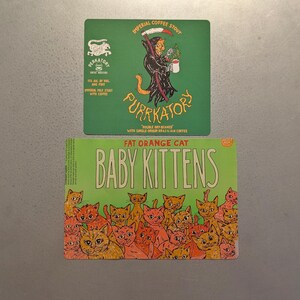 May include: Two beer coasters. The top one is green with a Grim Reaper-like figure holding a coffee cup, the text "PURRKATORY" and "IMPERIAL COFFEE STOUT". The bottom coaster is green with orange kittens and the text "FAT ORANGE CAT BABY KITTENS".