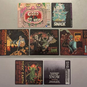 May include: Nine different craft beer labels featuring various illustrations and text. The labels are printed on a white background and feature a variety of colors, including black, white, red, green, blue, and yellow. The labels include text such as "Forbidden Pumpkin", "Toxic Earth", "Good as New", "Midnight Snack", "Pilgrimage into the Dank", "Wandering into the Snow", and "Isolation".