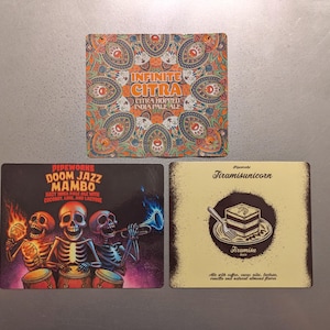 May include: Three square coasters with unique designs. One features a colorful paisley pattern with the text "Infinite Citra." Another has a skull band with the words "Doom Jazz Mambo." The last coaster displays a tiramisu graphic.