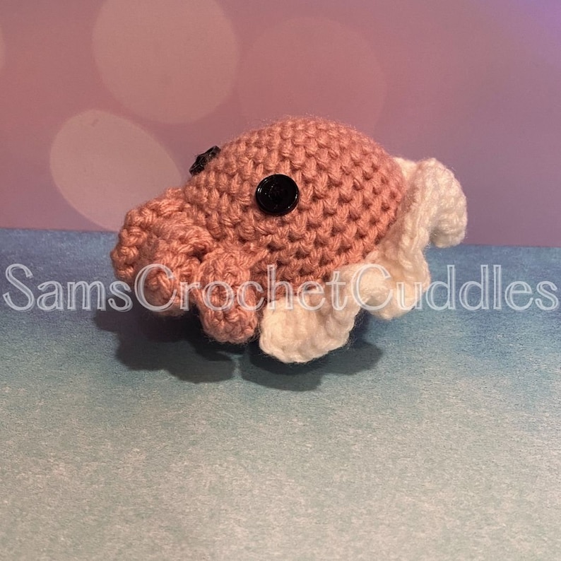 K&ouml;nnte beinhalten: Ein geh&auml;kelter rosa-wei&szlig;er Oktopus mit schwarzen Knopfaugen.