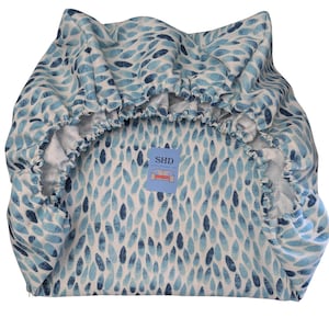 Puede incluir: Una funda de silla con estampado azul y blanco con borde elástico. La funda tiene una pequeña etiqueta azul con el texto "SHD" en ella.