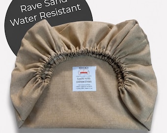 Pode incluir: Uma capa de almofada bege, elástica e resistente à água. A capa apresenta o texto "Rave Sand" e "Water Resistant" num círculo preto. O produto também tem uma etiqueta que diz "Elastic Fitted Cushion Covers".