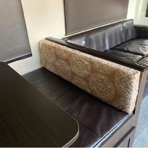 Könnte beinhalten: Ein braunes Ledersofa mit einem gemusterten Kissen. Das Sofa befindet sich in einem Wohnmobil oder Wohnwagen.