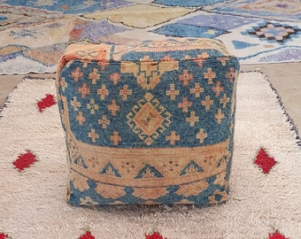 May include: A blue and orange patterned square pouf sits on a white fluffy rug with red diamond shapes.