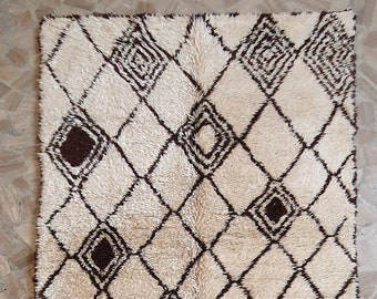 May include: A white and brown Moroccan rug with a geometric diamond pattern. The rug has a shaggy texture and a fringe border.