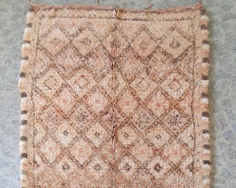 Puede incluir: Alfombra rectangular tejida a mano con un patrón geométrico de diamantes en tonos beige, marrón y rojo. La alfombra tiene un borde con flecos y probablemente está hecha de lana o una fibra natural similar. El diseño es simétrico y tradicional.