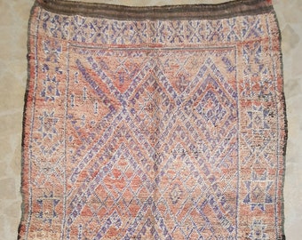 May include: A vintage Moroccan rug with a geometric pattern in shades of pink, purple, and white. The rug has a fringe border and is made of wool.