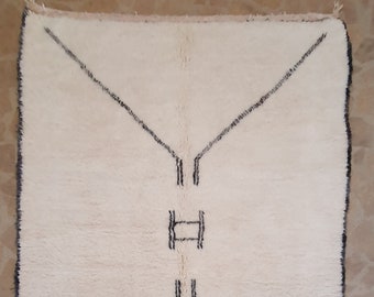 Könnte beinhalten: Ein weißer Teppich mit einem einfachen schwarzen geometrischen Muster. Der Teppich hat einen Fransenrand.