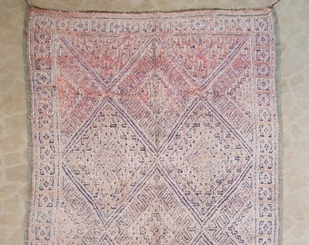 May include: A vintage Moroccan rug with a geometric pattern in shades of pink, beige, and purple. The rug has a fringe border and is in good condition.