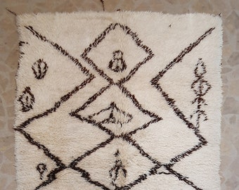 May include: A white Moroccan rug with a brown geometric pattern. The rug has a fringe border and is made of wool.