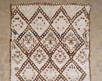 May include: A white and brown Moroccan rug with a geometric diamond pattern. The rug has a fringe border.