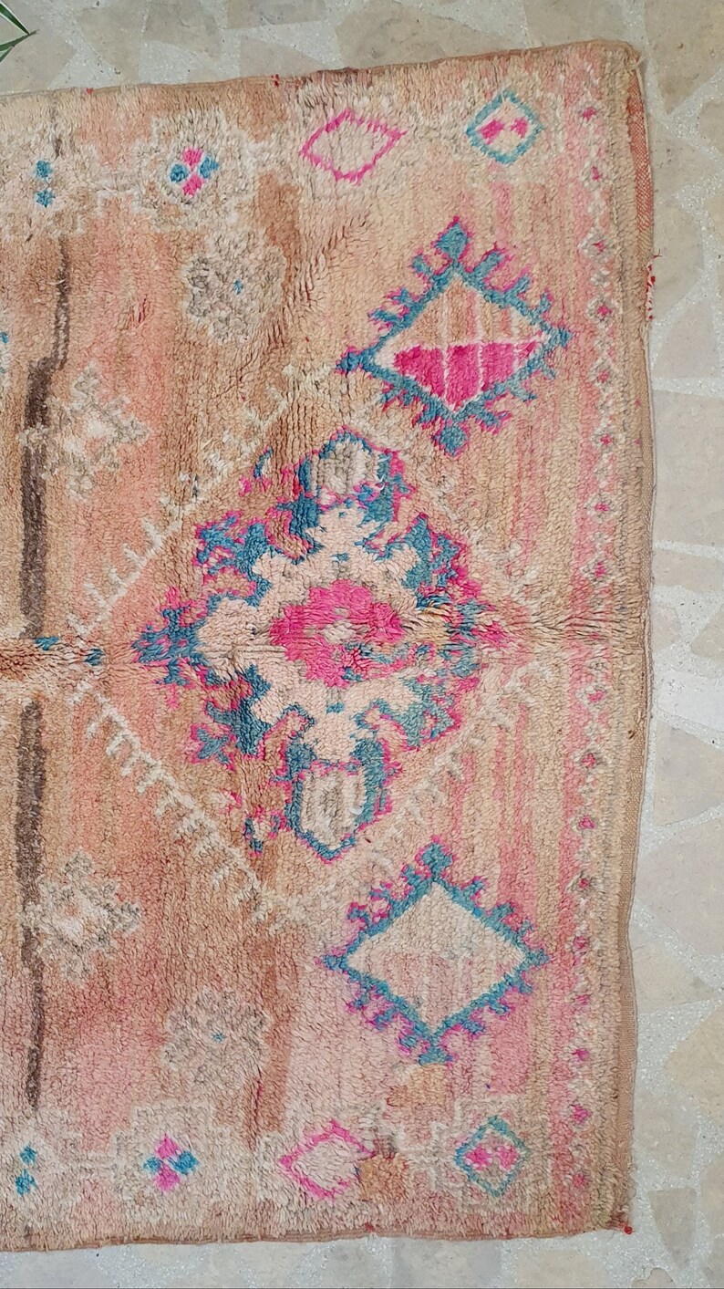 May include: A vintage Moroccan rug with a beige background and intricate patterns in shades of pink, blue, and white.
