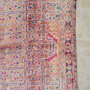 May include: A vintage Moroccan rug with a geometric pattern in shades of pink, purple, green, and white on a beige background.