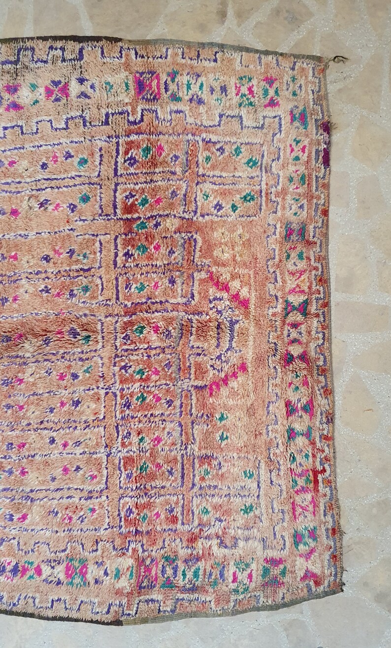 May include: A vintage Moroccan rug with a geometric pattern in shades of pink, purple, green, and white on a beige background.
