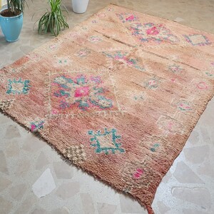 May include: A vintage Moroccan rug with a faded pink and beige background. The rug features a geometric pattern in shades of teal, pink, and white.