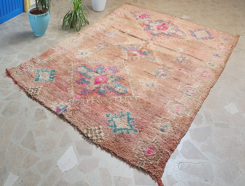 May include: A vintage Moroccan rug with a faded pink and beige background. The rug features a geometric pattern in shades of teal, pink, and white.