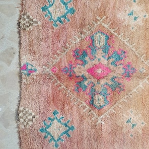 May include: A vintage Moroccan rug with a pink, beige and blue geometric pattern. The rug has a distressed look and is made of wool.