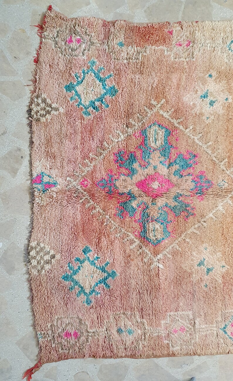 May include: A vintage Moroccan rug with a pink, beige and blue geometric pattern. The rug has a distressed look and is made of wool.