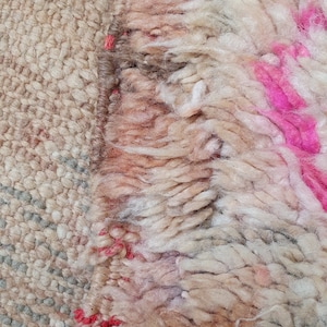 May include: Close-up of a beige and white rug with a pink and red fringe. The rug has a textured, woven look.