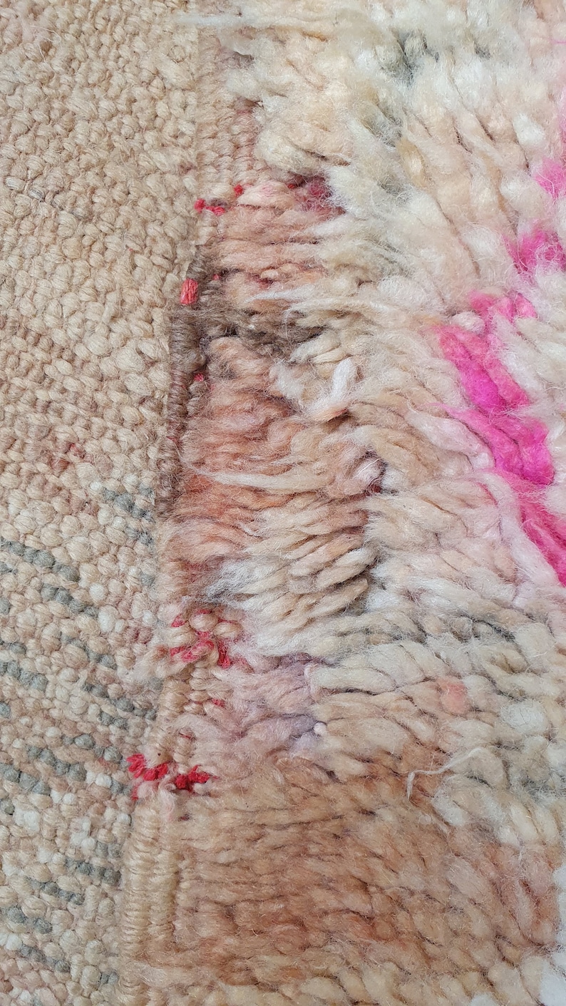 May include: Close-up of a beige and white rug with a pink and red fringe. The rug has a textured, woven look.