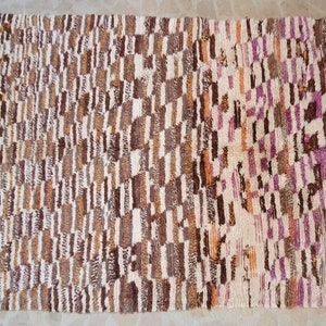 May include: A rectangular rug with a geometric pattern in shades of brown, white, and purple. The rug has a fringe border.