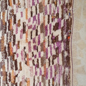 May include: A white, brown, orange, and purple Moroccan rug with a geometric pattern. The rug has a fringe border.